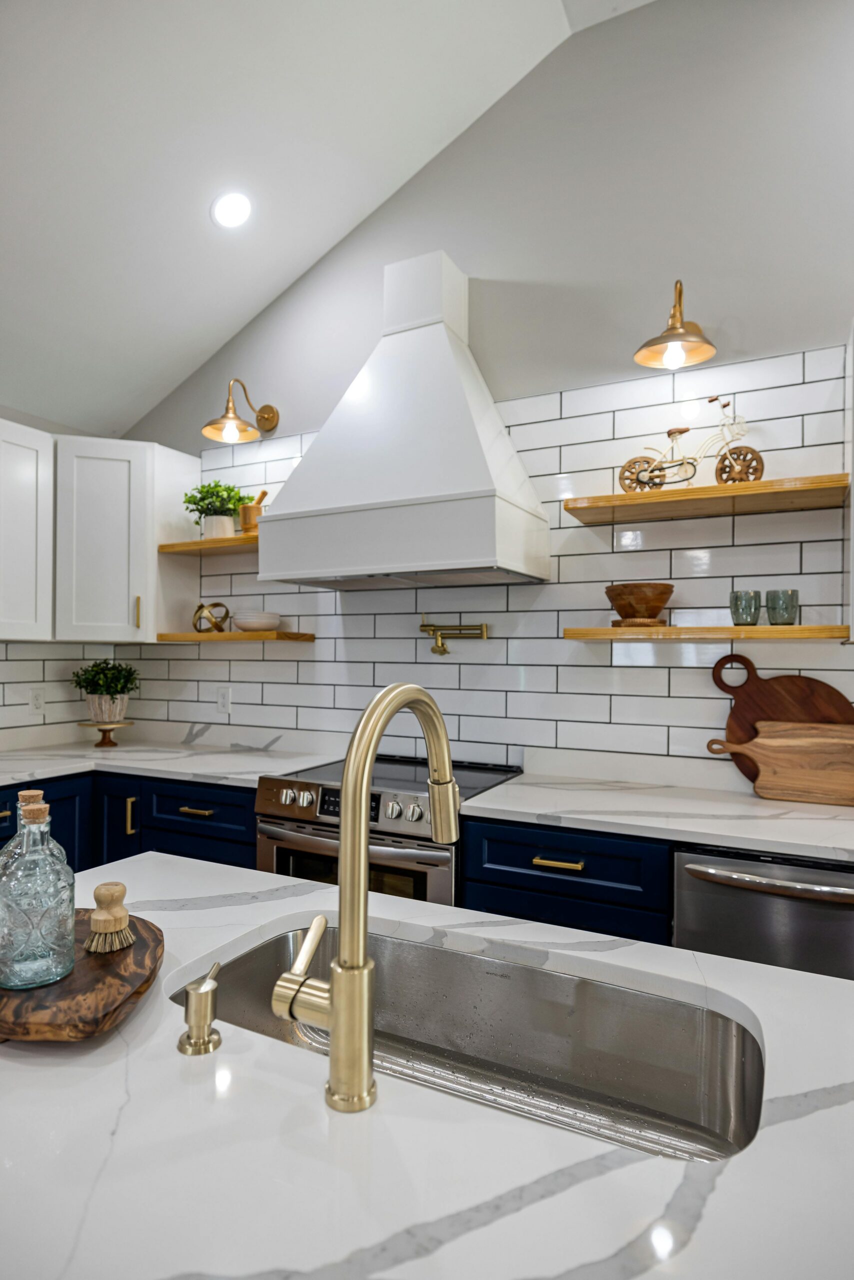 A contemporary luxury kitchen with gold fixtures, navy cabinets, and an elegant white backsplash.